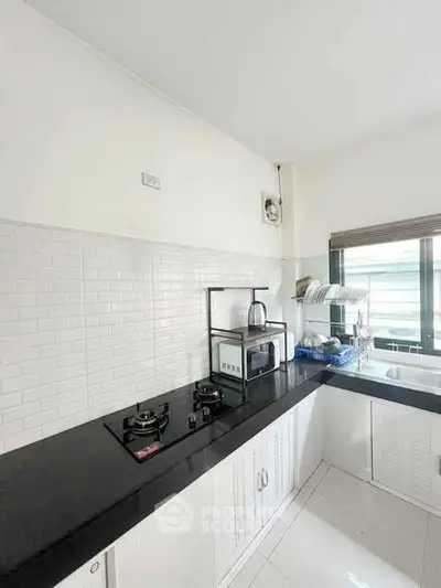 Modern kitchen with sleek black countertop and gas stove, featuring white cabinetry and ample natural light.