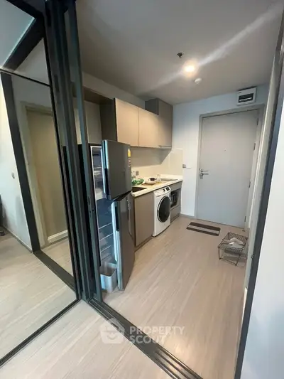 Modern compact kitchen with stainless steel appliances and washing machine in sleek apartment.