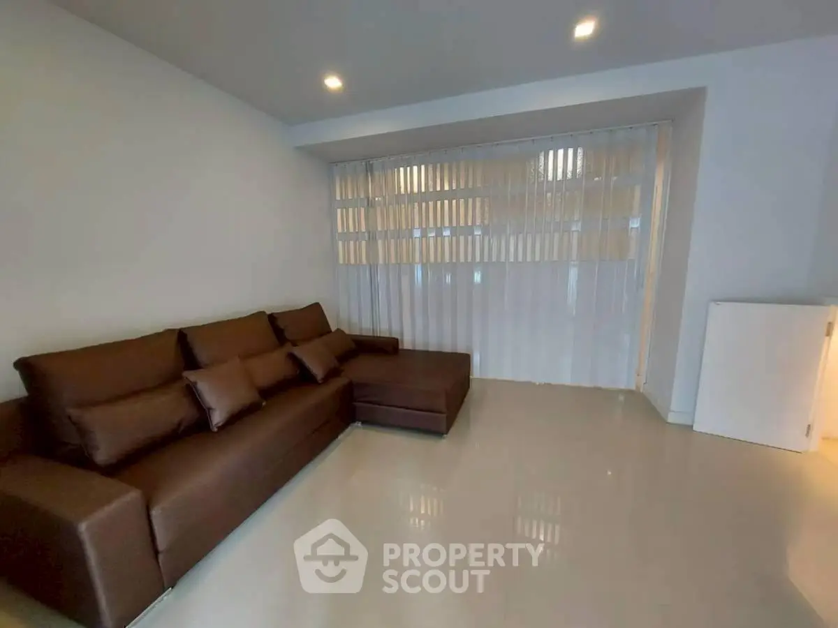 Spacious living room with modern brown sectional sofa and sleek tile flooring.