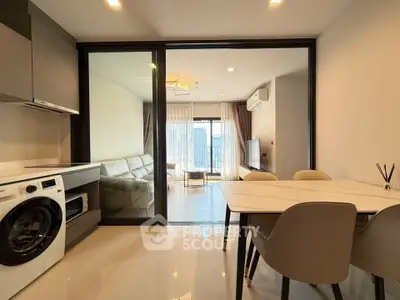 Modern open-plan living room with kitchen and city view, featuring sleek furniture and natural light.
