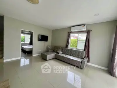 Spacious living room with modern sofa and wall-mounted TV, featuring large windows for natural light.