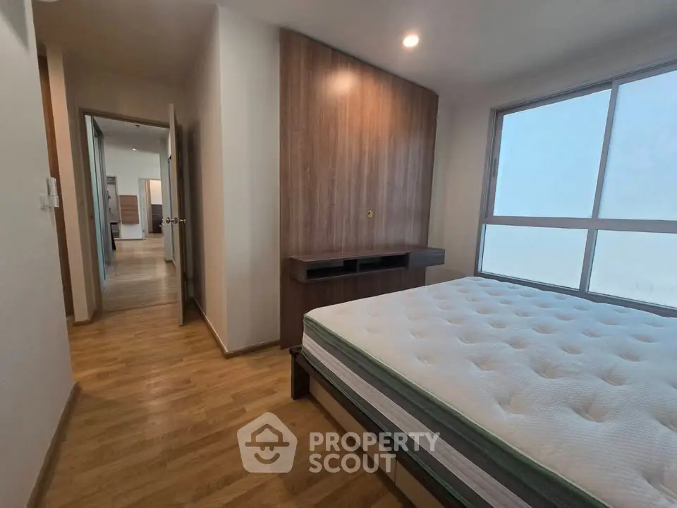 Spacious bedroom with wooden flooring and large window for natural light.
