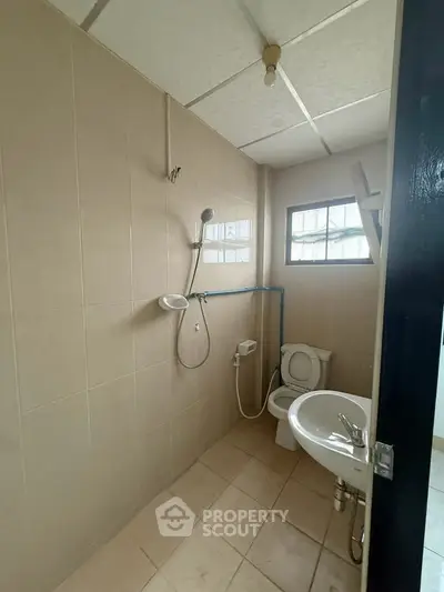 Compact bathroom with shower, toilet, and sink in a tiled setting.