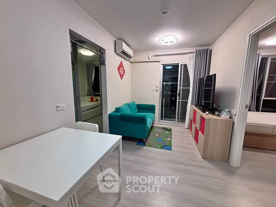 Modern living room with teal sofa, flat-screen TV, and dining area in open layout apartment.