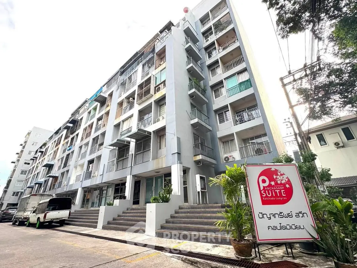 Modern multi-story apartment building with balconies and lush greenery in urban setting.