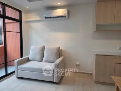Modern living room with cozy sofa and air conditioning, featuring natural light and sleek wooden cabinetry.