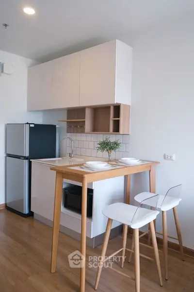 Modern kitchen with sleek design, featuring compact fridge, wooden breakfast bar, and stylish cabinetry.