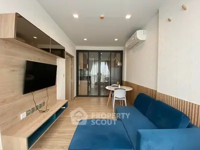 Modern living room with blue sofa and wall-mounted TV, open layout to kitchen area.