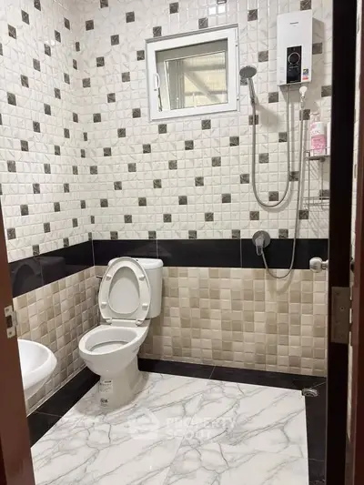 Modern bathroom with tiled walls and floor, featuring a toilet and shower setup.