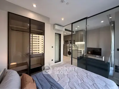 Modern bedroom with glass partition, view of sleek kitchen and living area.
