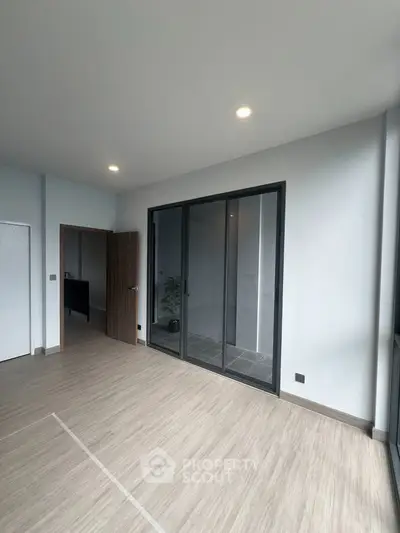 Spacious modern room with sliding glass doors and wood flooring, perfect for versatile living space.