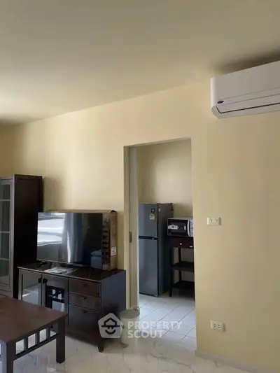 Modern living room with air conditioning and sleek furniture, featuring a TV and a glimpse of the kitchen area.