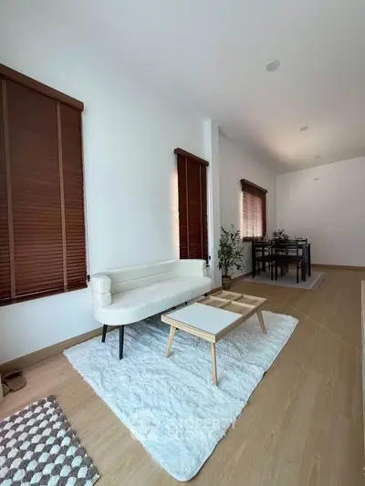 Modern living room with stylish furniture and wooden blinds, featuring a cozy white rug and elegant decor.