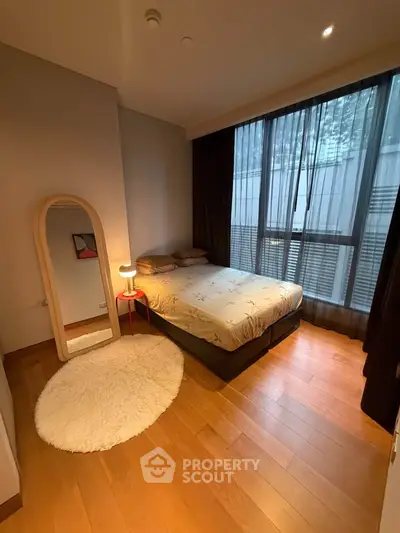 Cozy bedroom with wooden flooring, large window, and stylish decor in modern apartment.