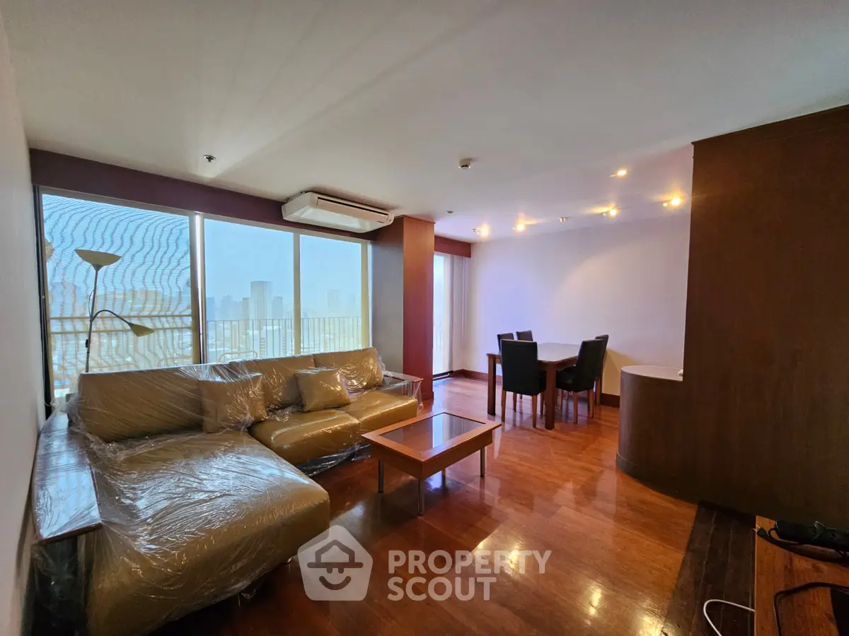 Spacious living room with large windows and modern furniture in a high-rise apartment.