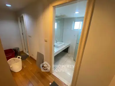 Spacious hallway leading to a modern bathroom with wooden flooring and sleek fixtures.