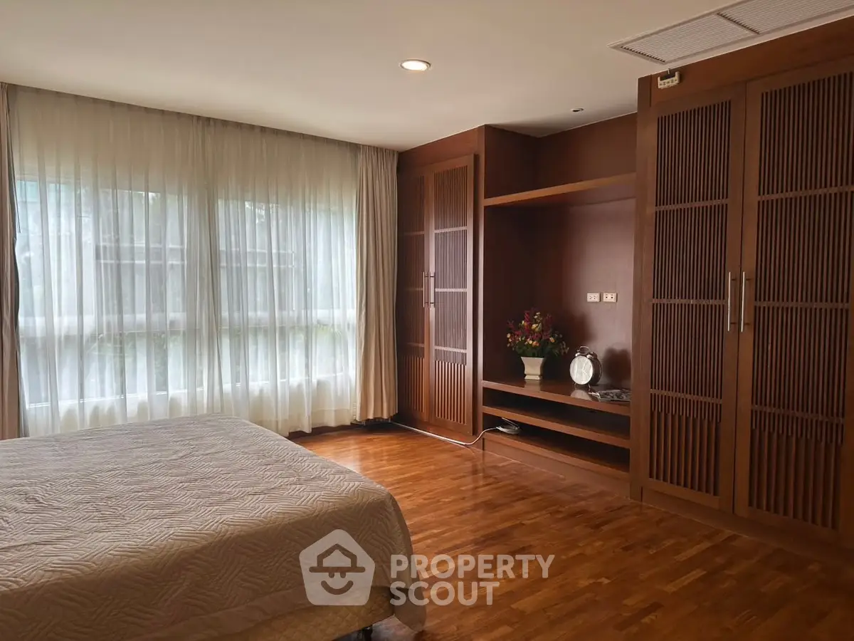 Spacious bedroom with elegant wooden flooring and large windows for natural light.