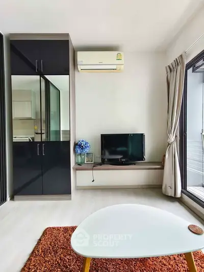 Modern living room with sleek furniture and natural light, featuring a TV and air conditioning unit.
