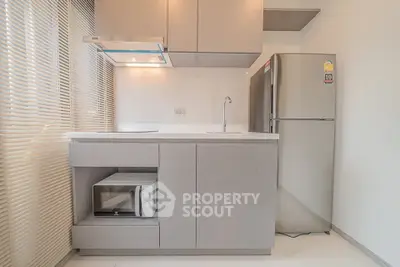 Modern kitchen with sleek cabinetry, stainless steel fridge, and built-in microwave in a compact layout.