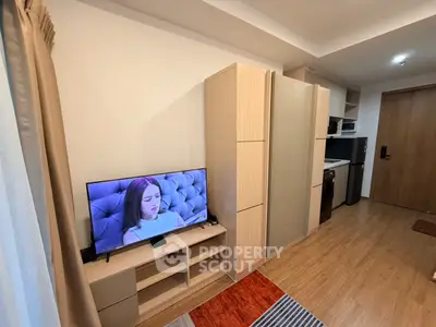Modern studio apartment with stylish furniture and flat-screen TV, featuring a compact kitchen area.