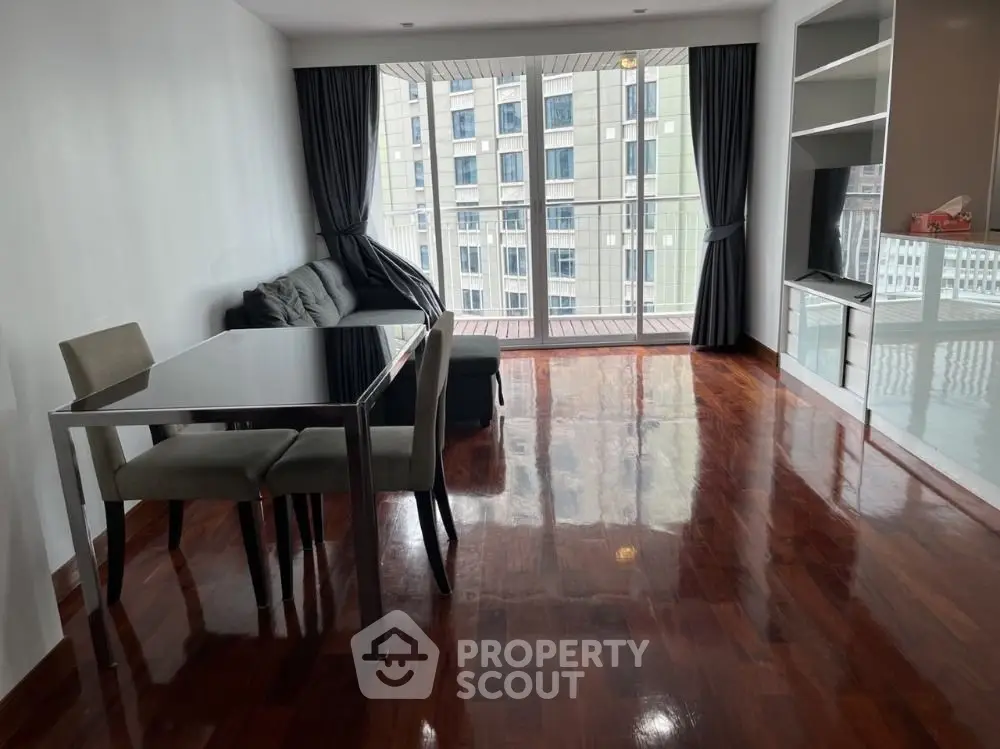 Spacious living room with polished wooden floors and large windows offering city views.