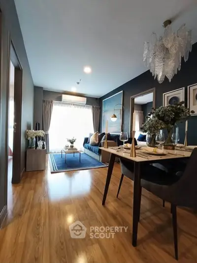 Elegant living room with modern decor and dining area, featuring a stylish chandelier and wooden flooring.