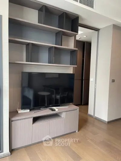 Modern living room with sleek TV unit and open shelving, featuring contemporary design and warm wood flooring.