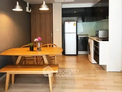 Modern kitchen with dining area, featuring wooden table, chairs, fridge, and washing machine.