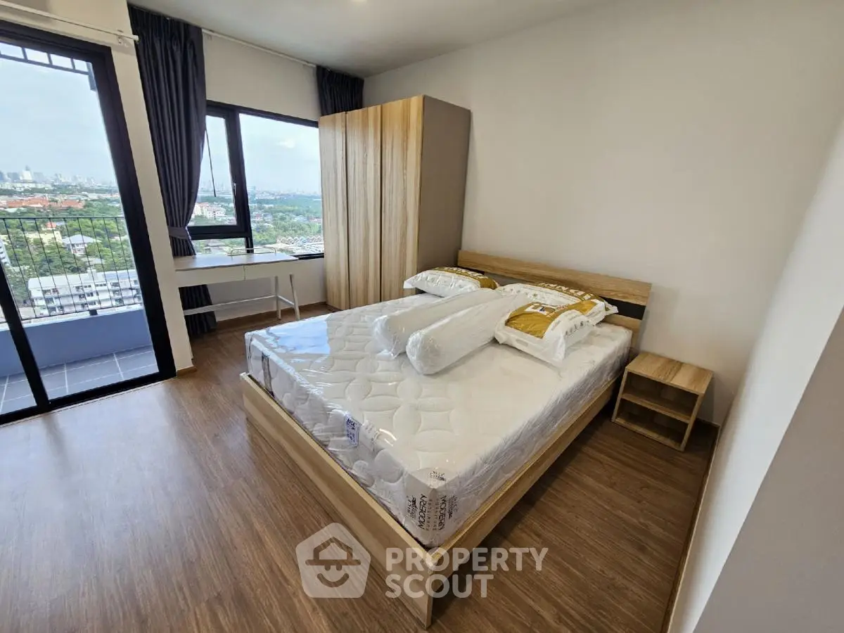 Modern bedroom with large window and city view, featuring a comfortable bed and wooden flooring.