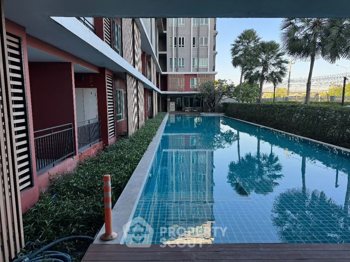 Modern apartment building with a serene poolside view and lush greenery.