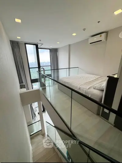 Modern loft bedroom with glass railing and city view, featuring sleek design and natural light.