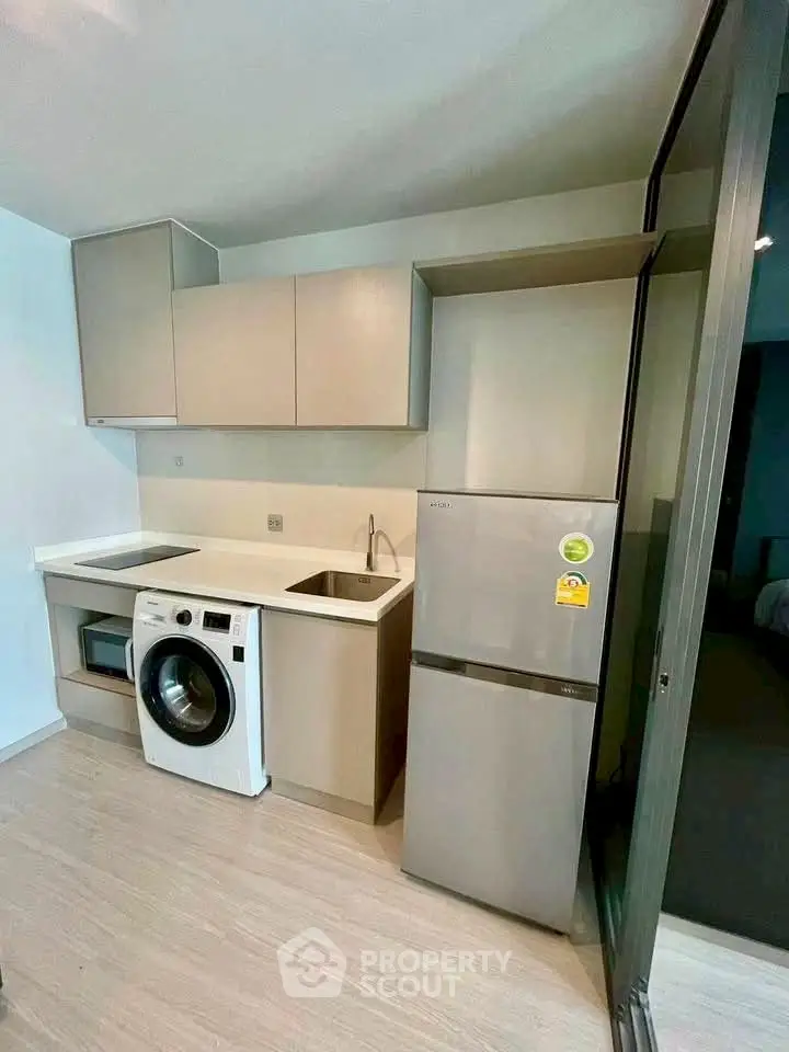 Modern compact kitchen with washing machine and fridge in sleek apartment.