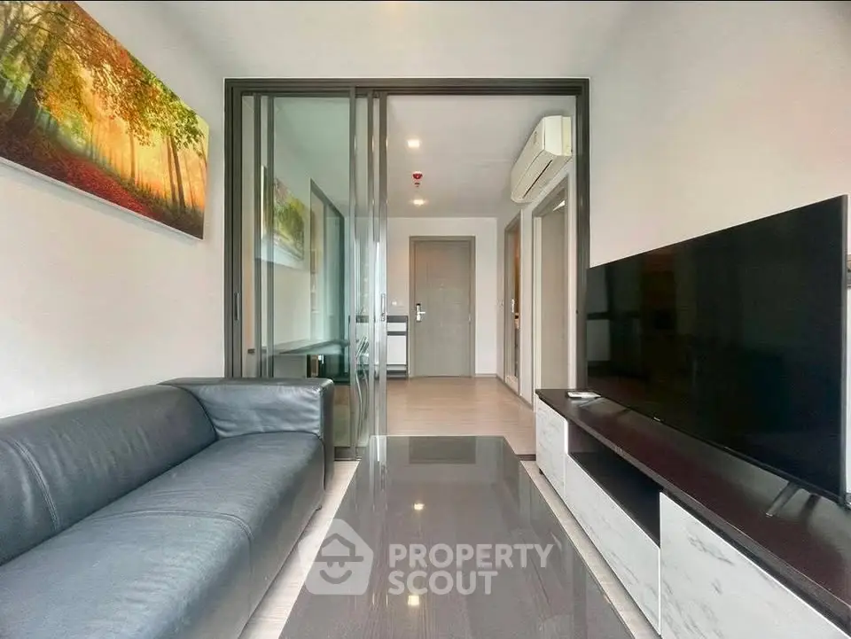 Modern living room with sleek black sofa, large TV, and stylish decor in a contemporary apartment.