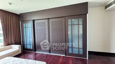 Elegant bedroom with wooden sliding doors and large windows, featuring a cozy sofa and hardwood floors.