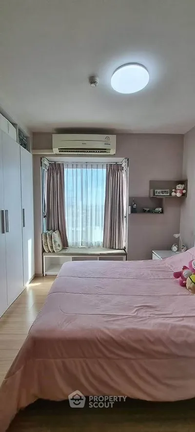Cozy bedroom with large window and pink bedding, featuring ample storage and natural light.