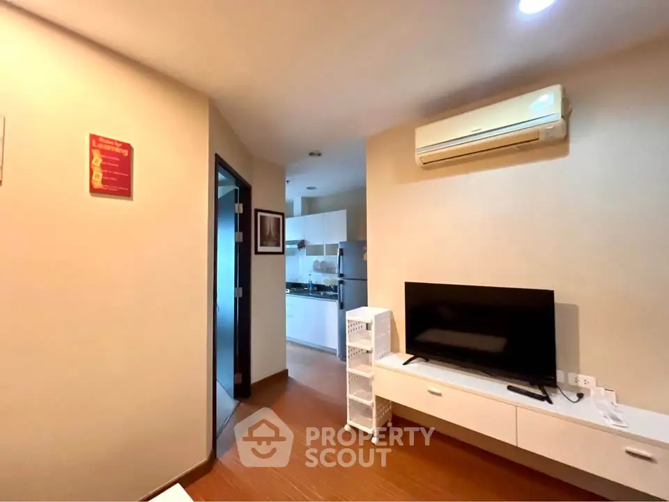 Modern living room with TV and air conditioning, leading to a sleek kitchen area.