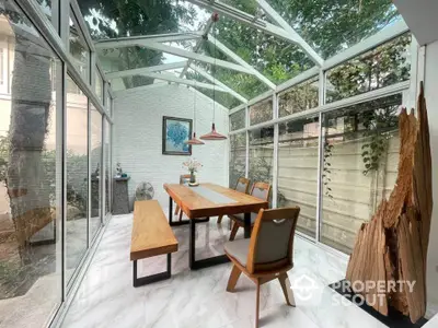 Stunning glass-enclosed dining area with modern wooden furniture and lush garden views.