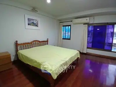 Spacious bedroom with wooden flooring and large window for natural light.