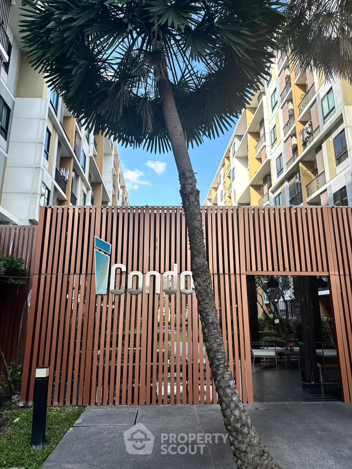Modern condo entrance with stylish wooden facade and lush palm tree.