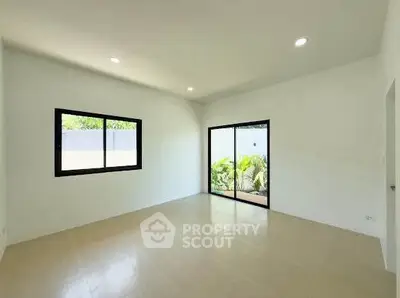Spacious empty room with large windows and sliding glass door to garden view.