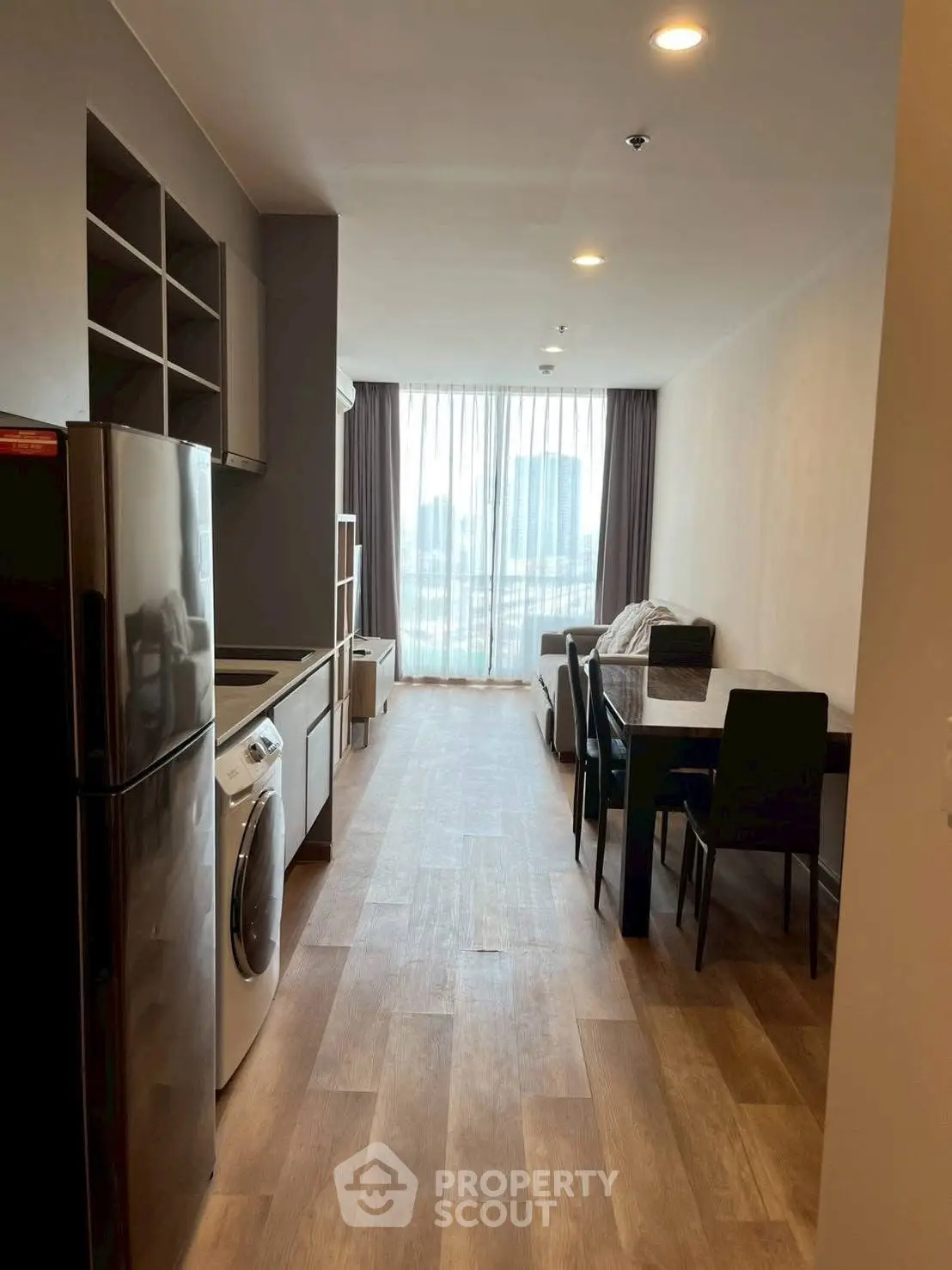 Modern apartment interior with open kitchen and dining area, featuring wooden flooring and large windows.