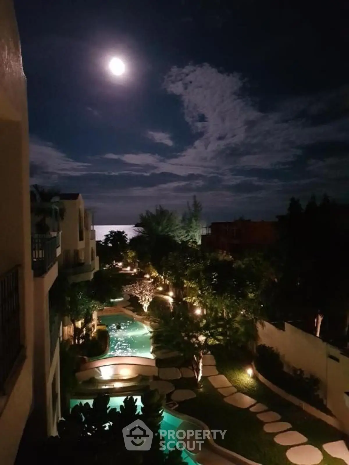 Stunning night view of luxury property with illuminated pool and lush garden under moonlight.