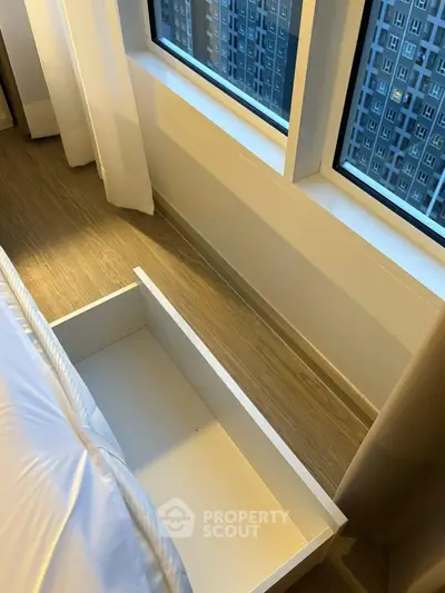 Modern bedroom with large windows and built-in storage drawer under bed, offering city views.