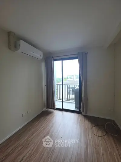 Spacious room with wooden flooring and balcony access, featuring a modern air conditioning unit.