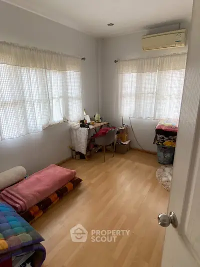 Cozy bedroom with natural light and wooden flooring, featuring a compact workspace and air conditioning.