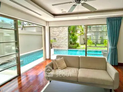 Luxurious living room with pool view and modern decor, featuring large windows and elegant furnishings.