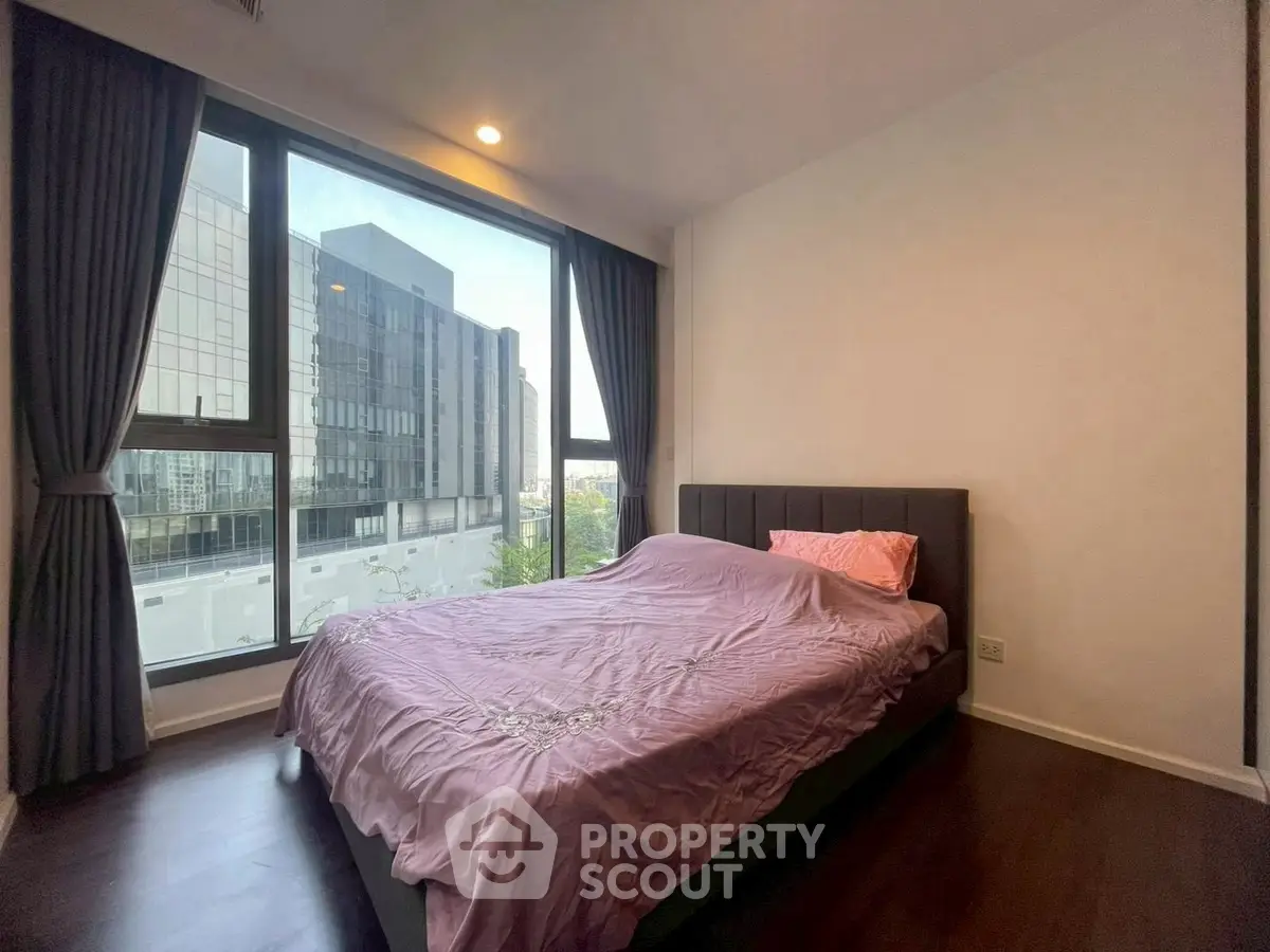 Modern bedroom with large window and city view, featuring elegant curtains and stylish bed.