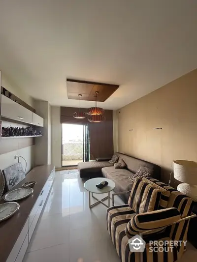 Elegant open-layout living room seamlessly connects to a modern kitchen, featuring chic lighting fixtures and a cozy balcony with natural light.