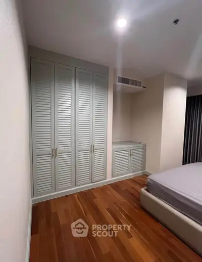 Spacious bedroom with elegant wooden flooring and built-in wardrobe in modern apartment.