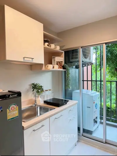 Modern kitchen with sleek cabinets and balcony view, featuring compact appliances and lush greenery outside.